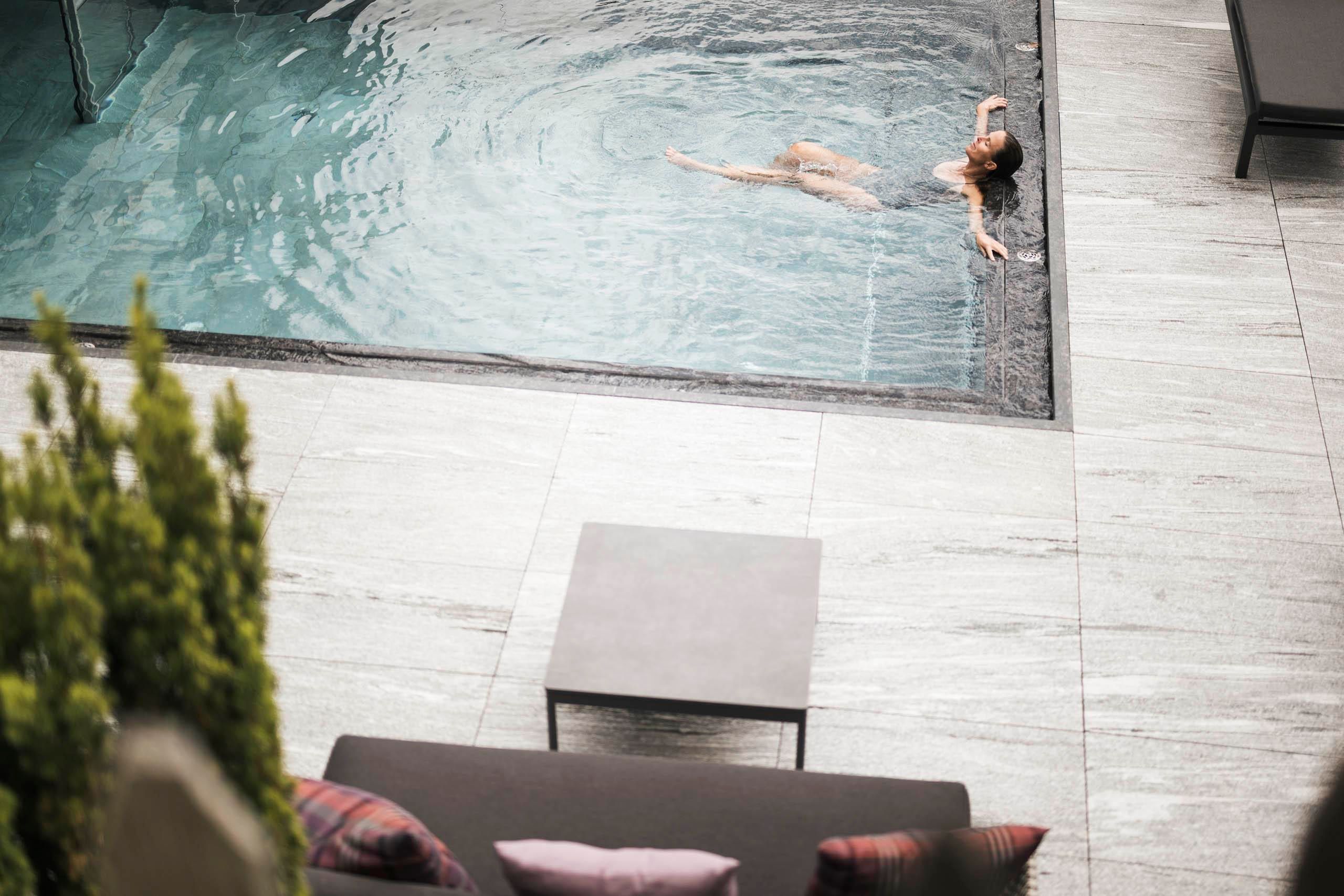 Ein eleganter Außenbereich mit Liegen und Sonnenschirmen, umgeben von Bäumen und Bergen. Der Pool reflektiert die Sonne und bietet eine entspannende Atmosphäre.