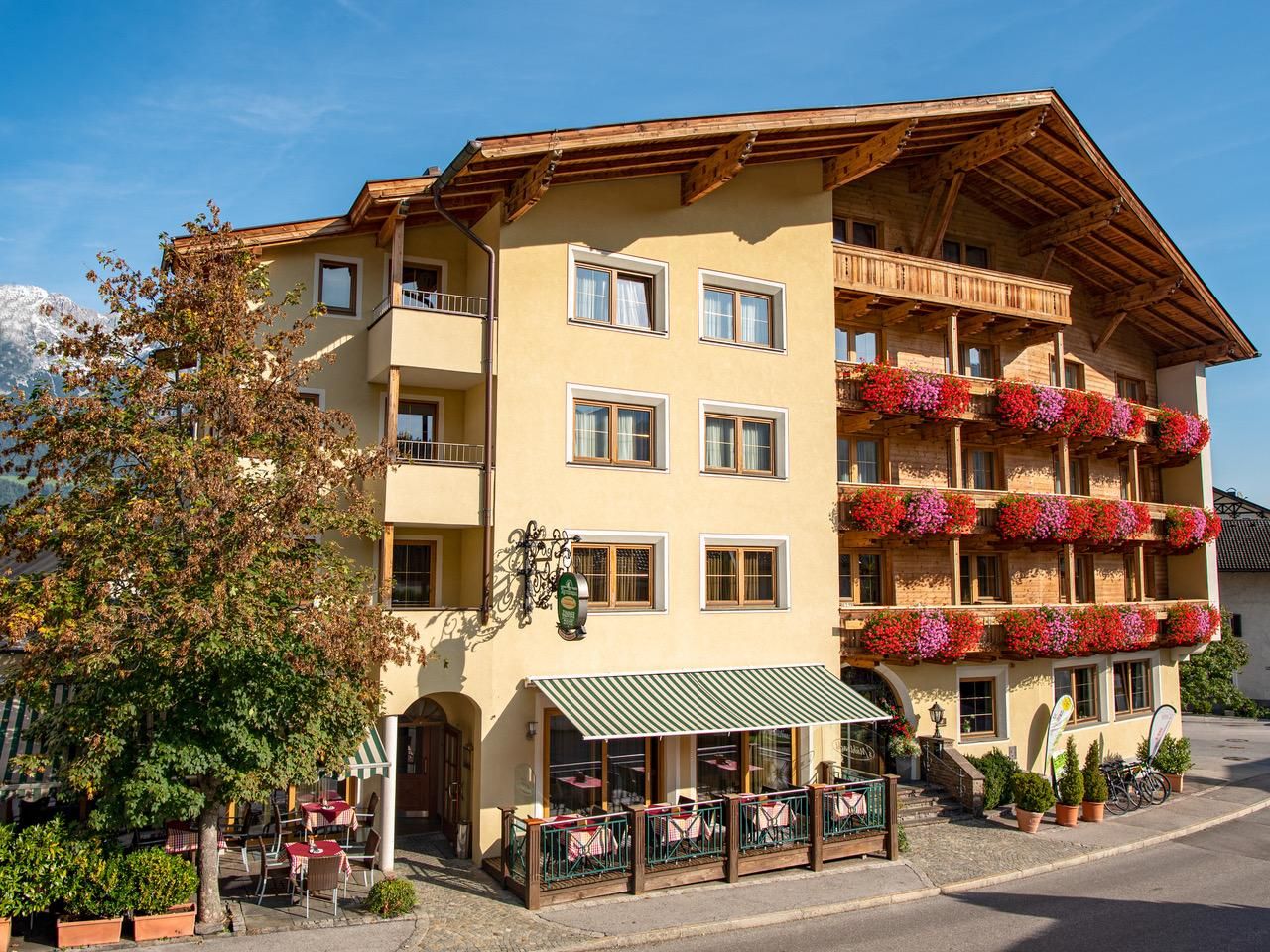 Ein charmantes Gebäude mit mehreren Balkonen, die mit bunten Blumen geschmückt sind. Vor dem Haus gibt es eine Terrasse mit Tischen und Stühlen.