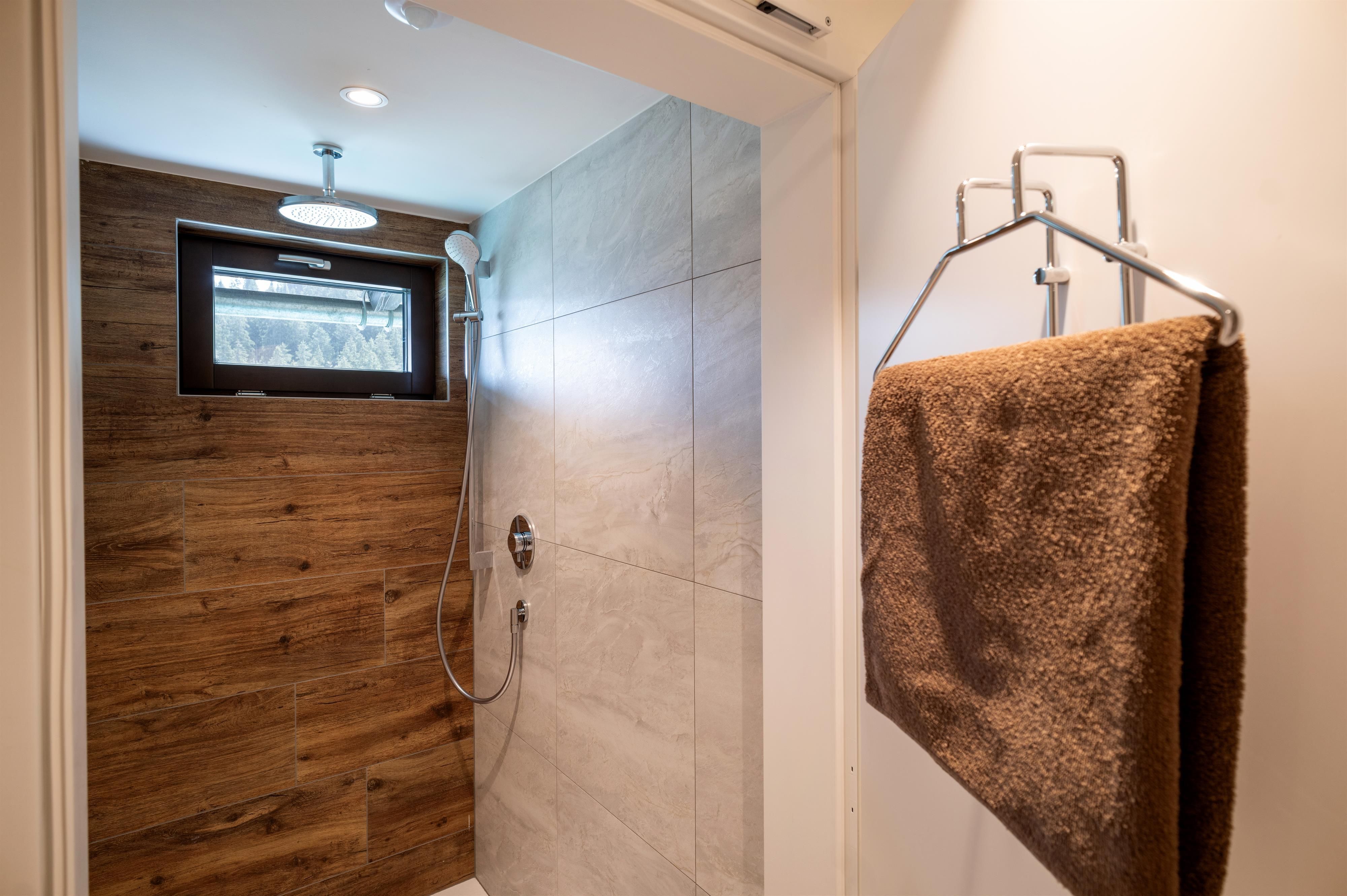 Eine moderne Dusche mit Fliesen und einer Holzverkleidung. Ein Handtuch hängt an einem Haken in der Ecke.