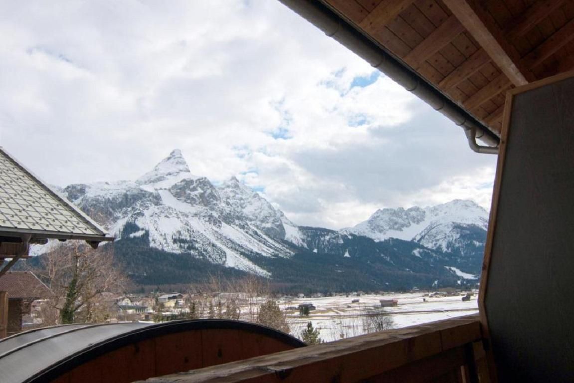 Ein Blick auf schneebedeckte Berge unter einem wolkigen Himmel. In der Landschaft sind einige Gebäude und Bäume zu sehen.
