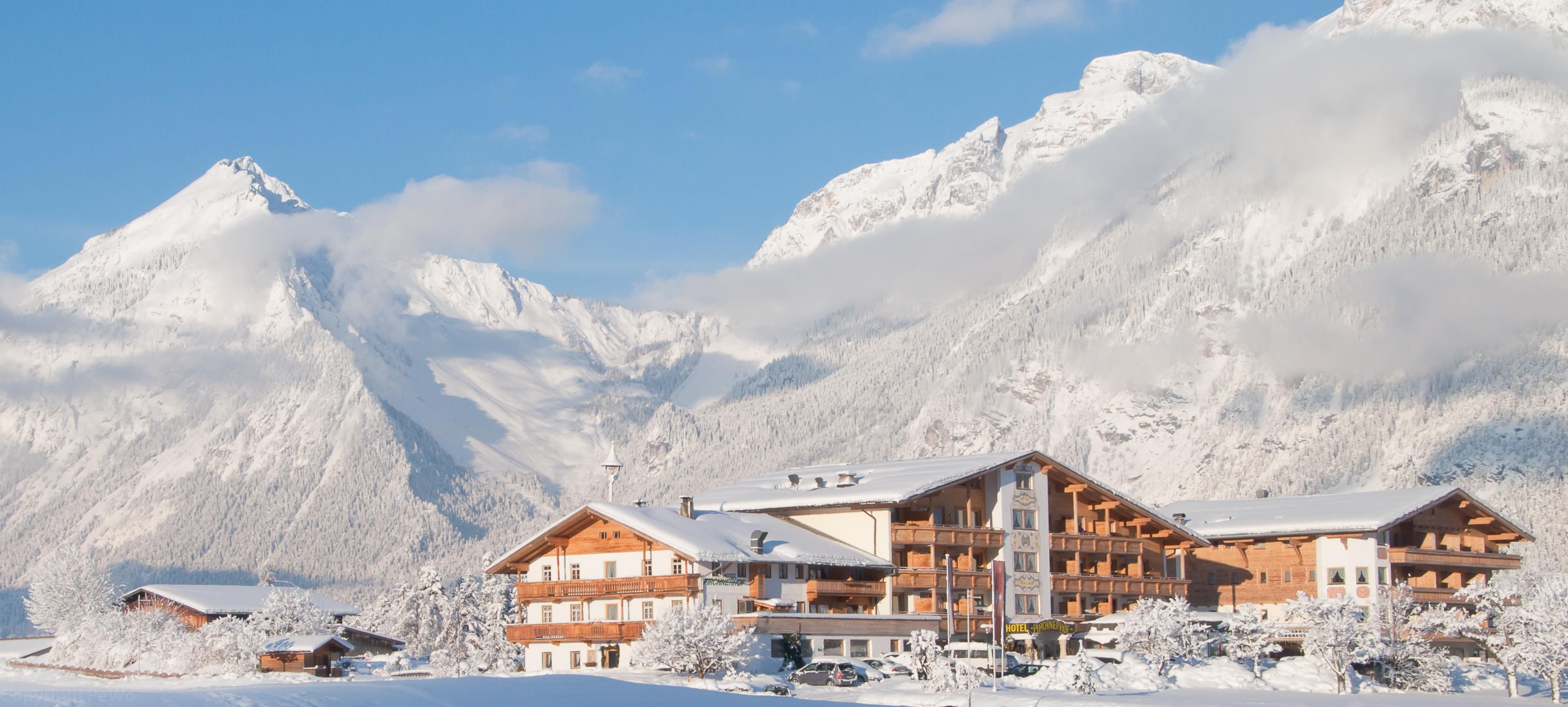 Ein malerisches Hotel in einem verschneiten Gebirgstal. Die umliegenden Berge sind mit Schnee bedeckt und der Himmel ist klar und blau.
