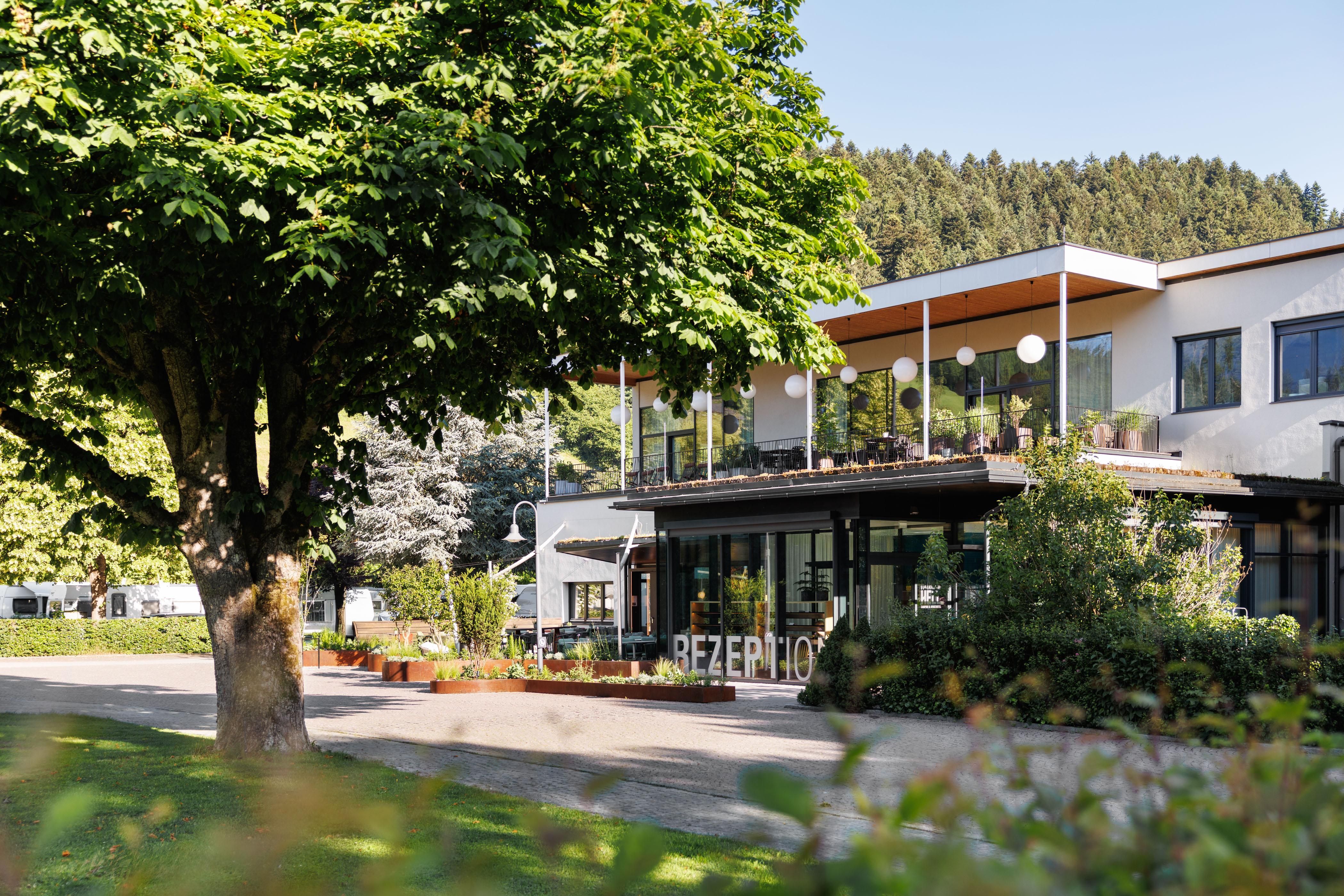 Ein modernes Gebäude mit einem Empfangsbereich. Umgeben von Bäumen und grüner Landschaft.