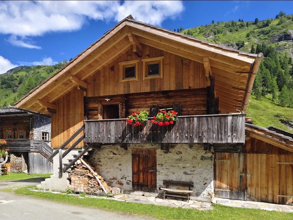 Eine traditionelle Almhütte in den Bergen mit blühenden Balkonblumen.