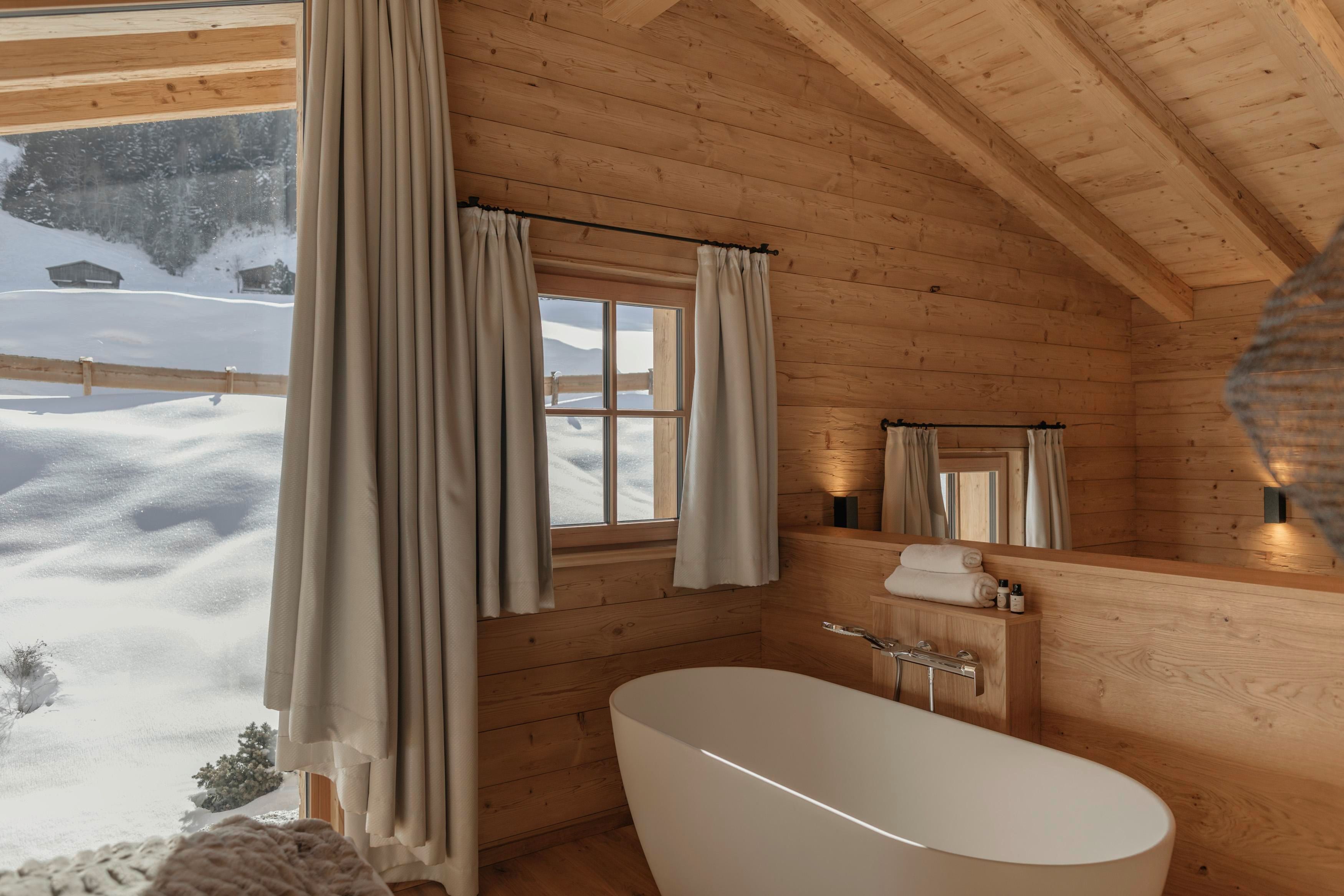Ein modernes Badezimmer aus Holz mit einer freistehenden Badewanne. Große Fenster bieten einen Blick auf die schneebedeckte Landschaft.