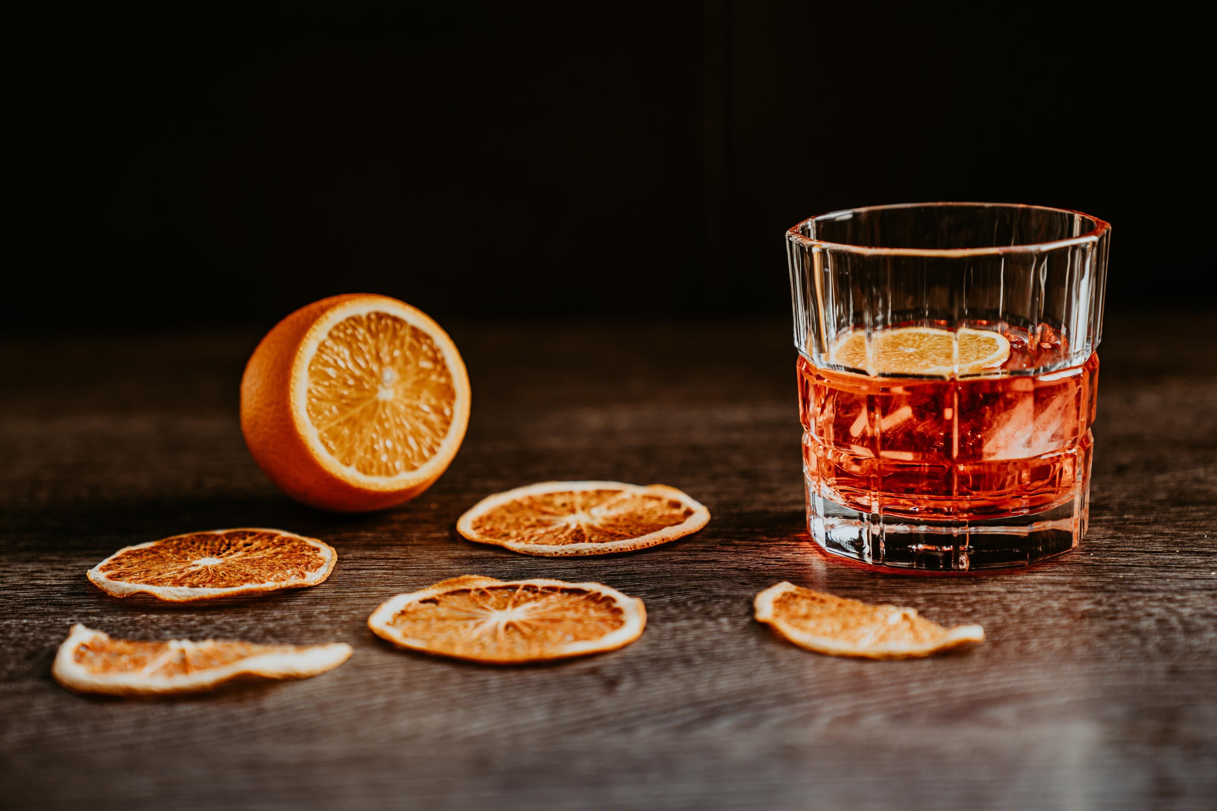 Ein Glas mit einem orangefarbenen Getränk und Zitrusfrüchten. Dörrobstscheiben liegen auf einem Holztisch verstreut.