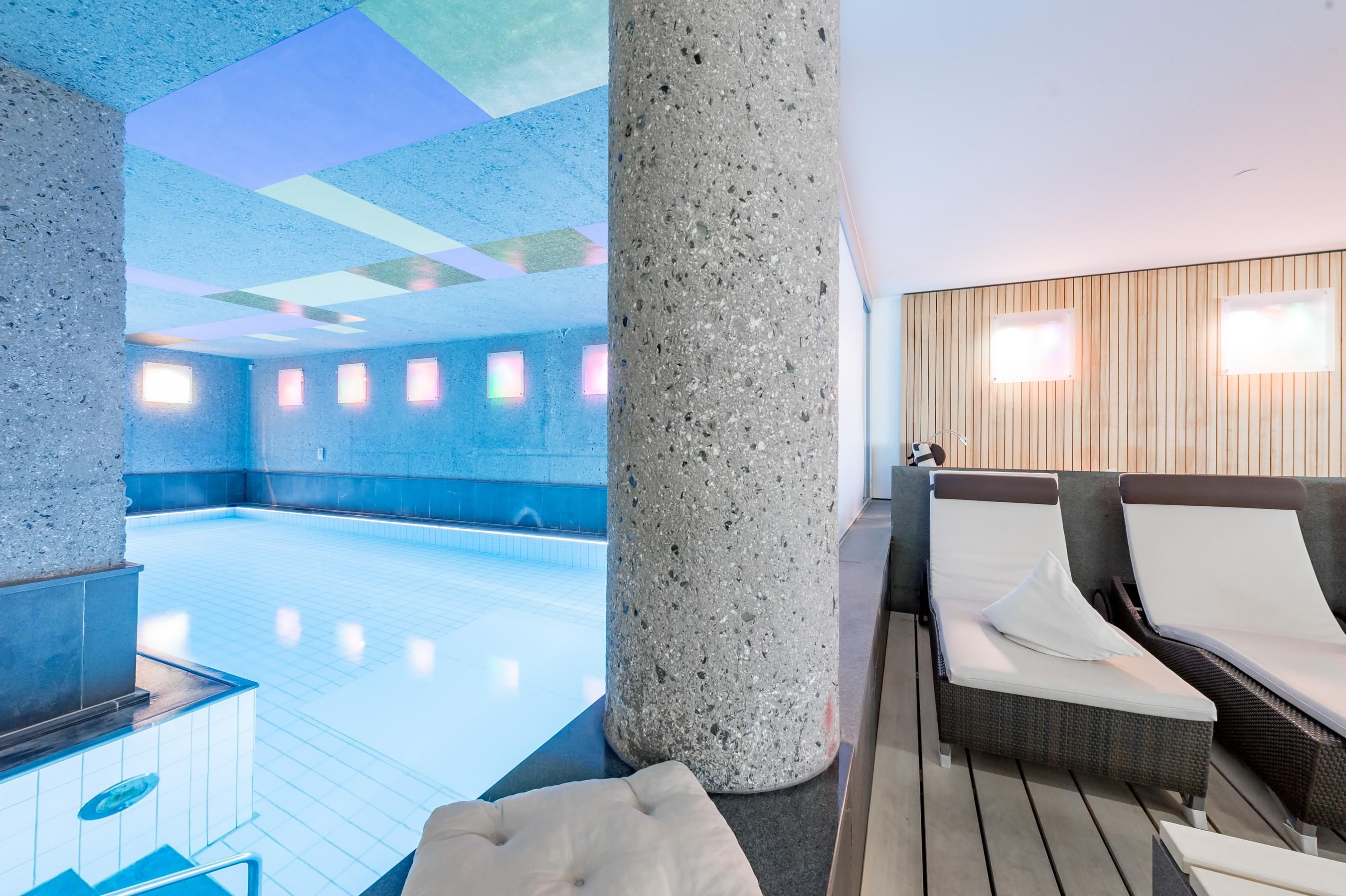 Ein eleganter Innenpool mit modernen Liegen und sanfter Beleuchtung. Die Wände sind in neutralen Tönen gehalten, was eine entspannende Atmosphäre schafft.
