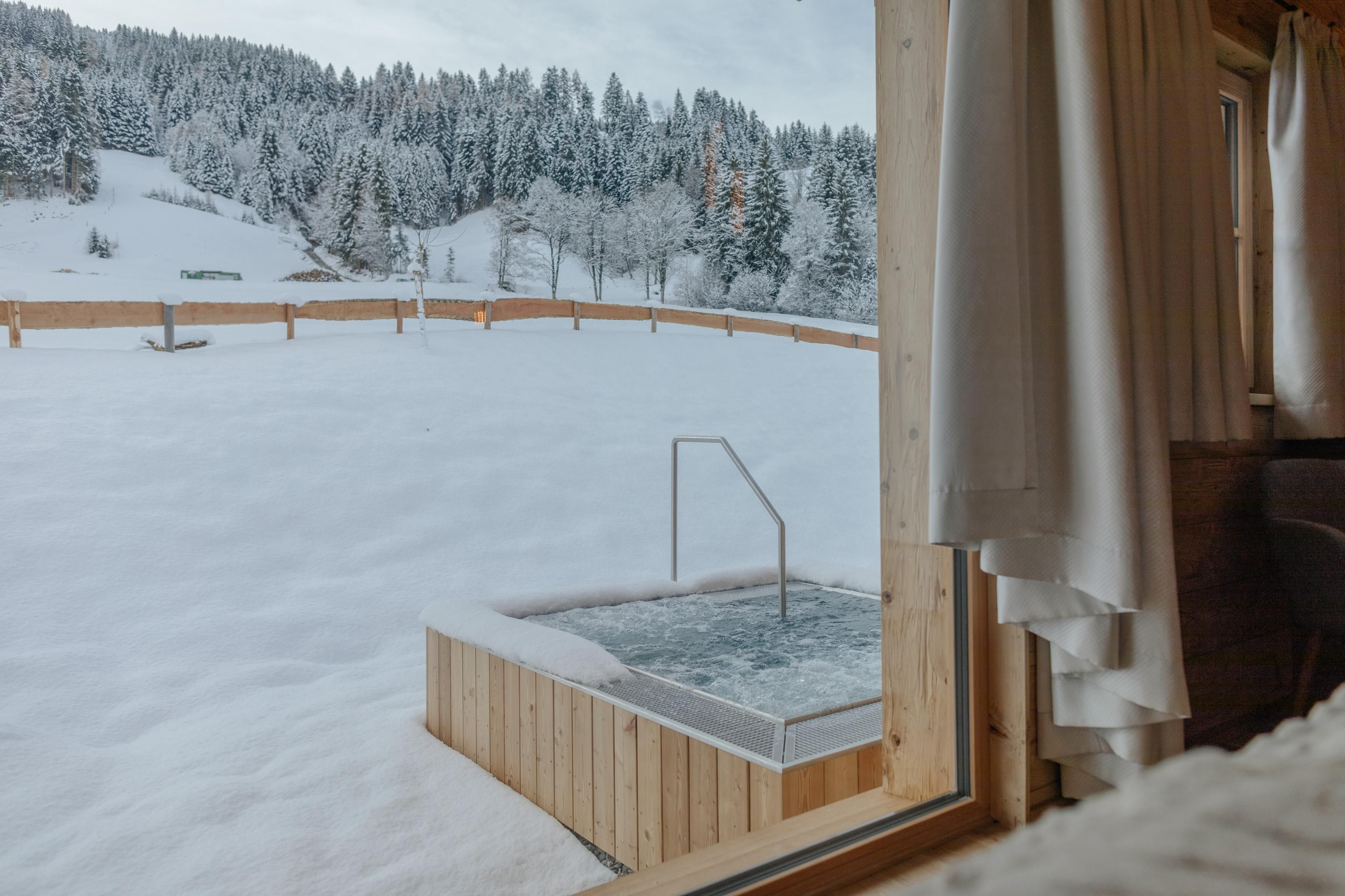 Ein Aussicht auf einen schneebedeckten Garten mit einem Holzspa. Die Bäume im Hintergrund sind winterlich bedeckt.