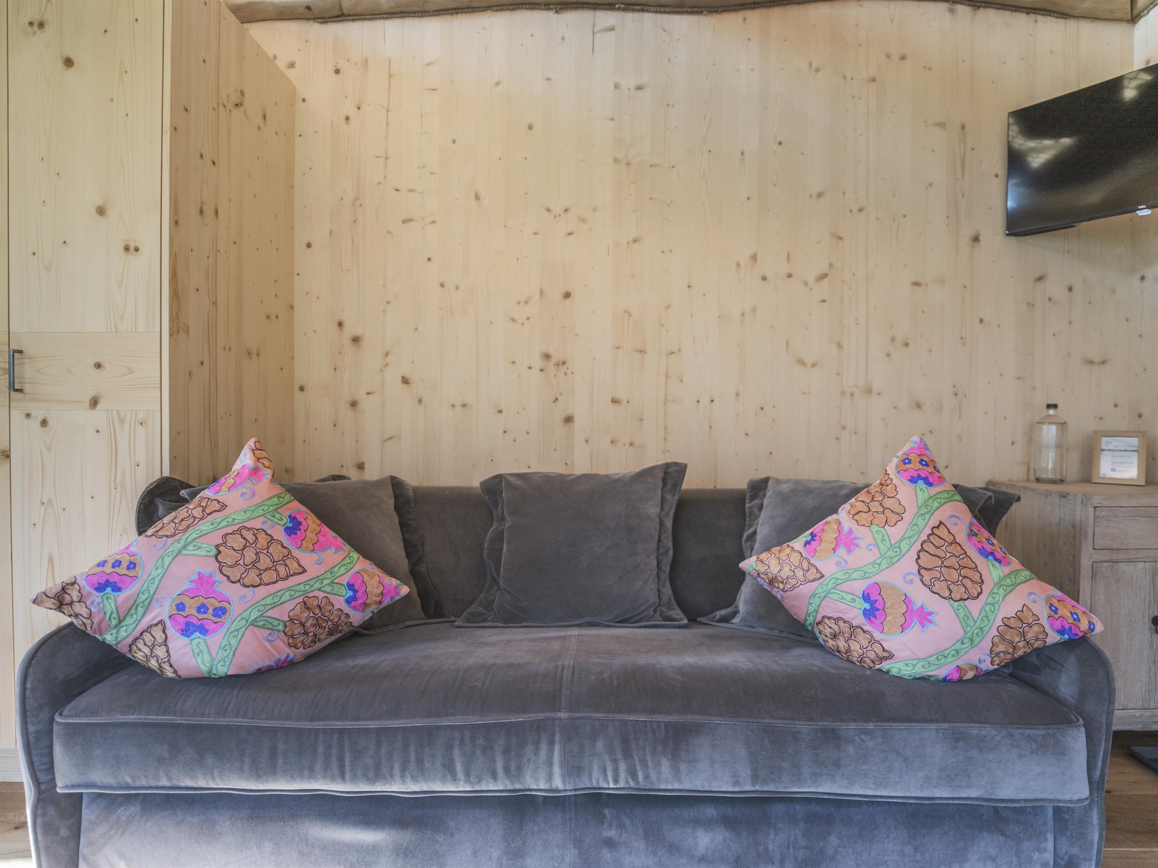 Ein gemütliches Sofa mit bunten Kissen in einem Raum mit Holzvertäfelung. An der Wand ist ein Fernseher montiert.
