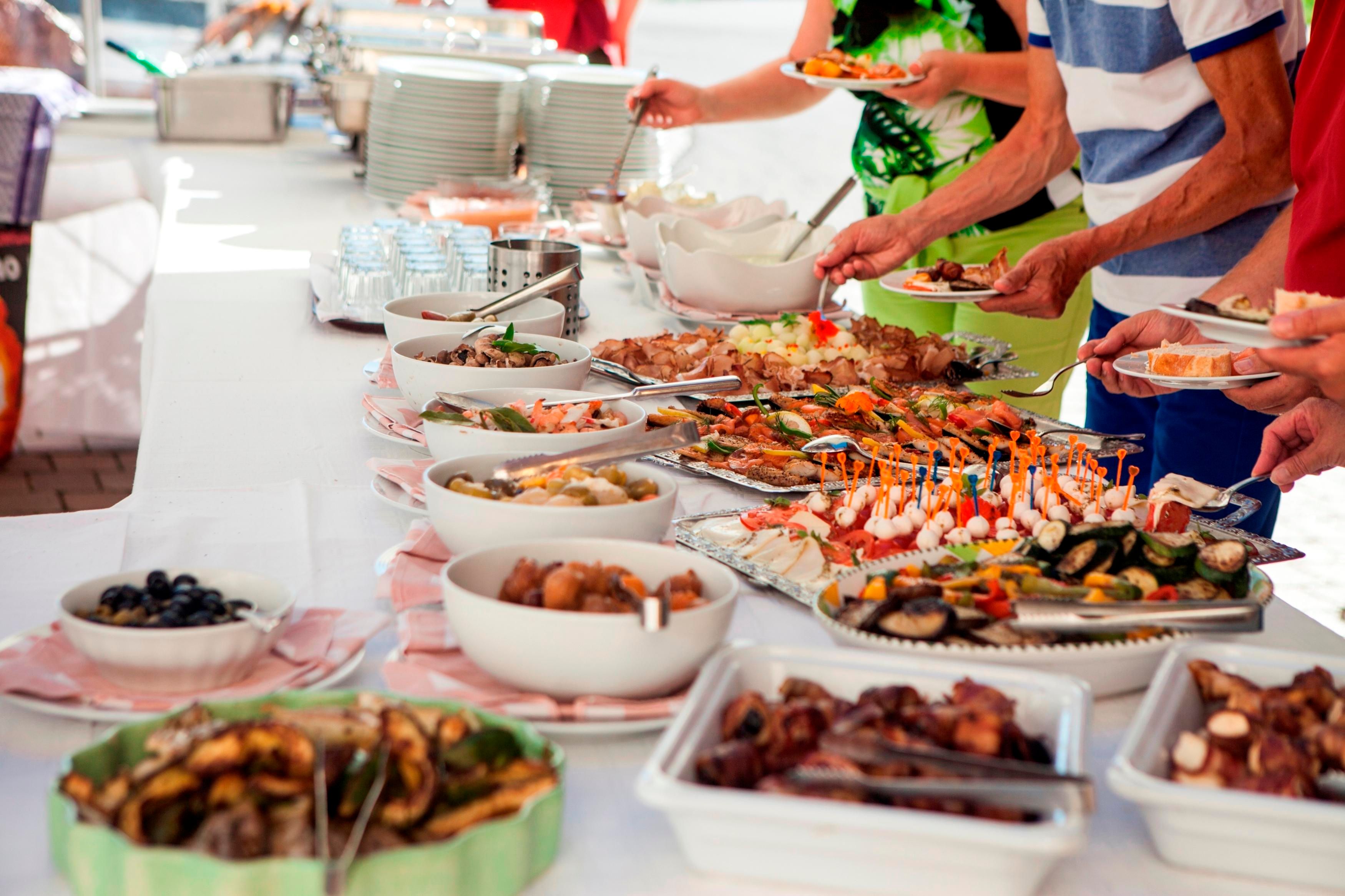 Ein reichhaltiges Buffet mit verschiedenen Gerichten, darunter Meeresfrüchte und Vorspeisen. Menschen bedienen sich an einer langen Tafel.