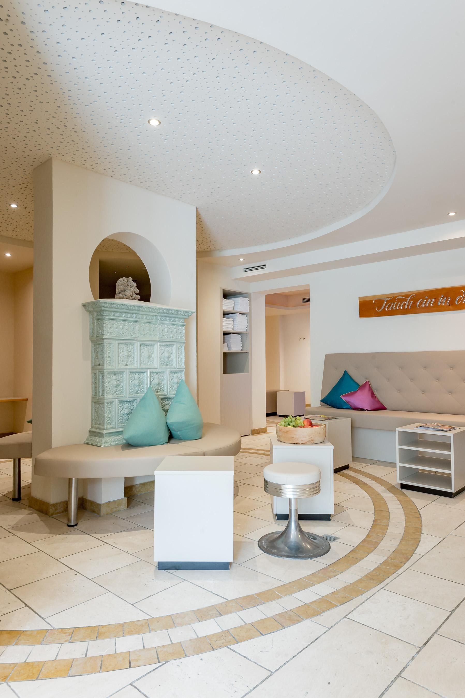 Ein modernes, helles Wartezimmer mit bequemen Bänken und Kissen. An der Wand befindet sich ein dekorativer Kamin.