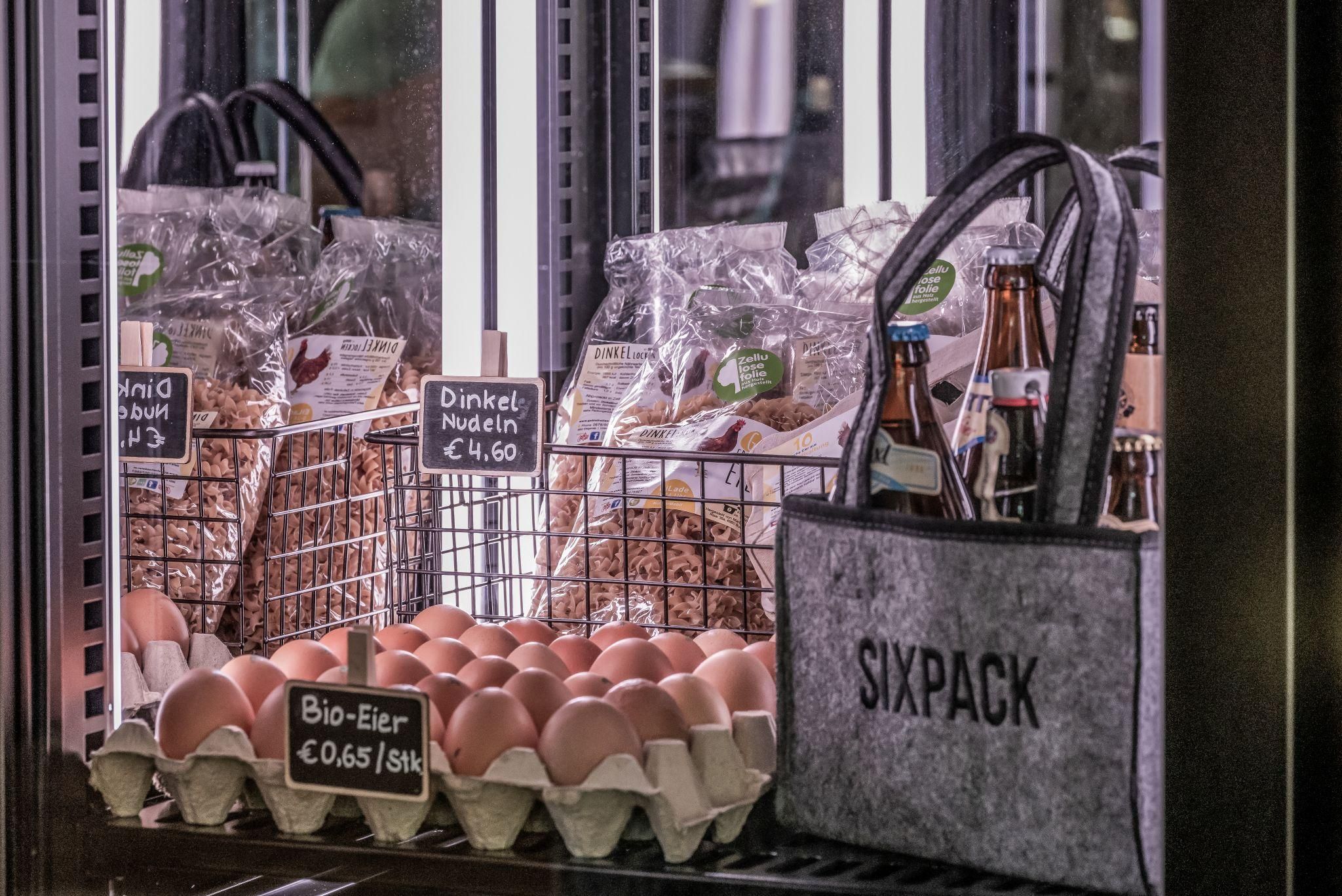 Im Kühlregal sind frische Bio-Eier und verschiedene Nudeln zu sehen. Daneben steht eine Tasche mit dem Aufdruck "SIXPACK".