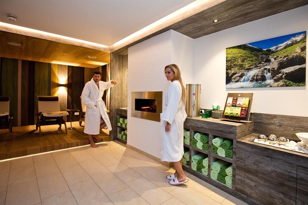 Ein luxuriöser Spa-Bereich mit gemütlichen Liegen und sanftem Licht. Zwei Personen in Bademänteln stehen in einem warmen, einladenden Raum.