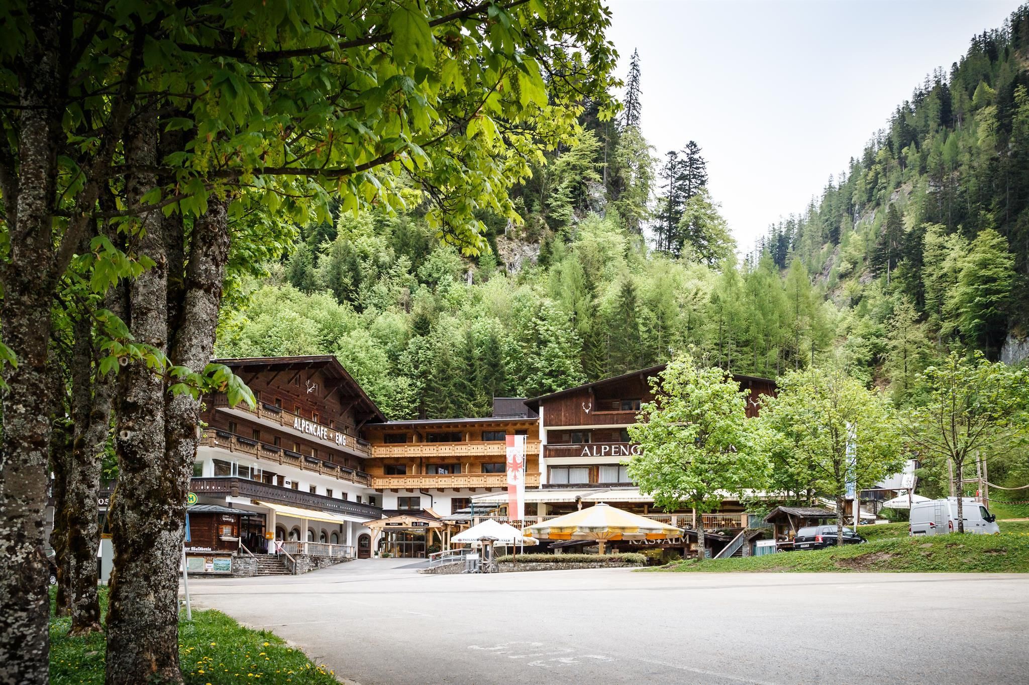 Ein gemütliches Hotel umgeben von Bäumen und Bergen. Die Terrasse lädt zum Verweilen ein.