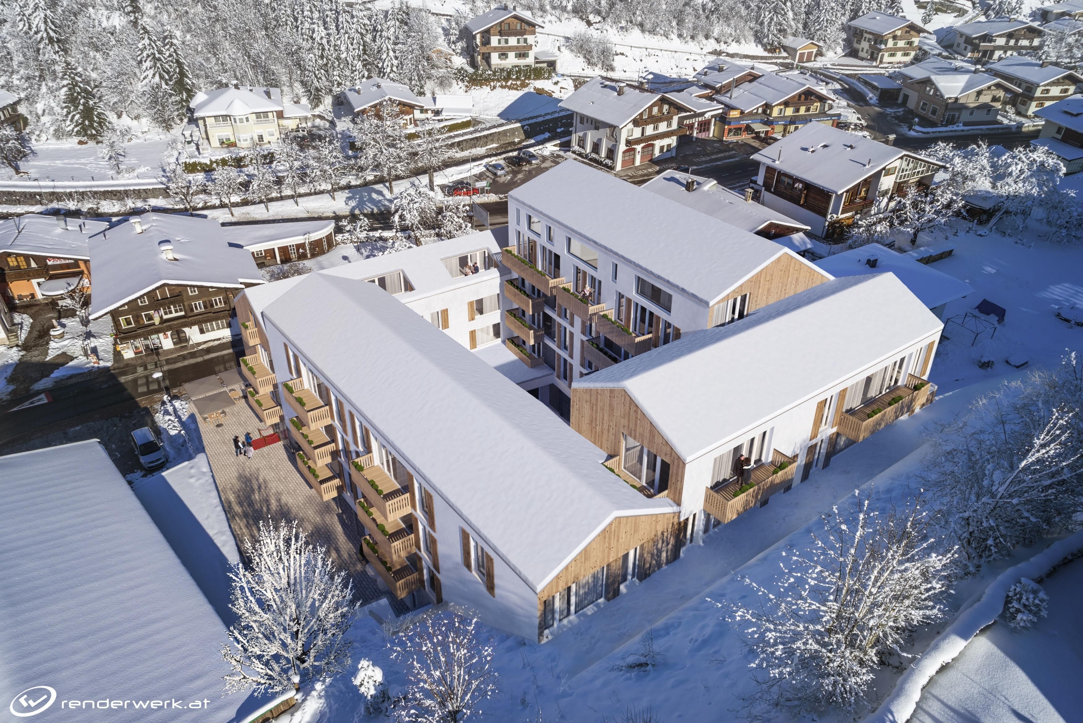 Ein schneebedecktes Dorf mit modernen Gebäuden und traditionellen Chalets. Die Umgebung ist idyllisch und ruhig in einer winterlichen Landschaft.