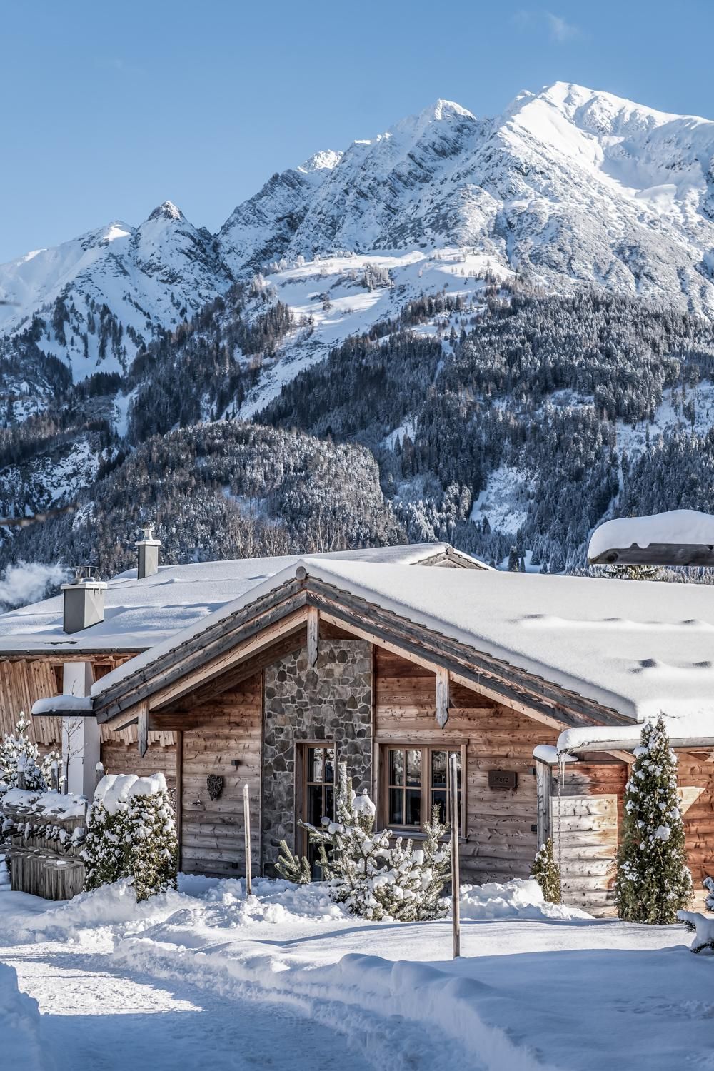 Ein gemütliches Chalet im Schnee, umgeben von schneebedeckten Bergen. Der Himmel ist klar und blau, was die winterliche Atmosphäre unterstreicht.