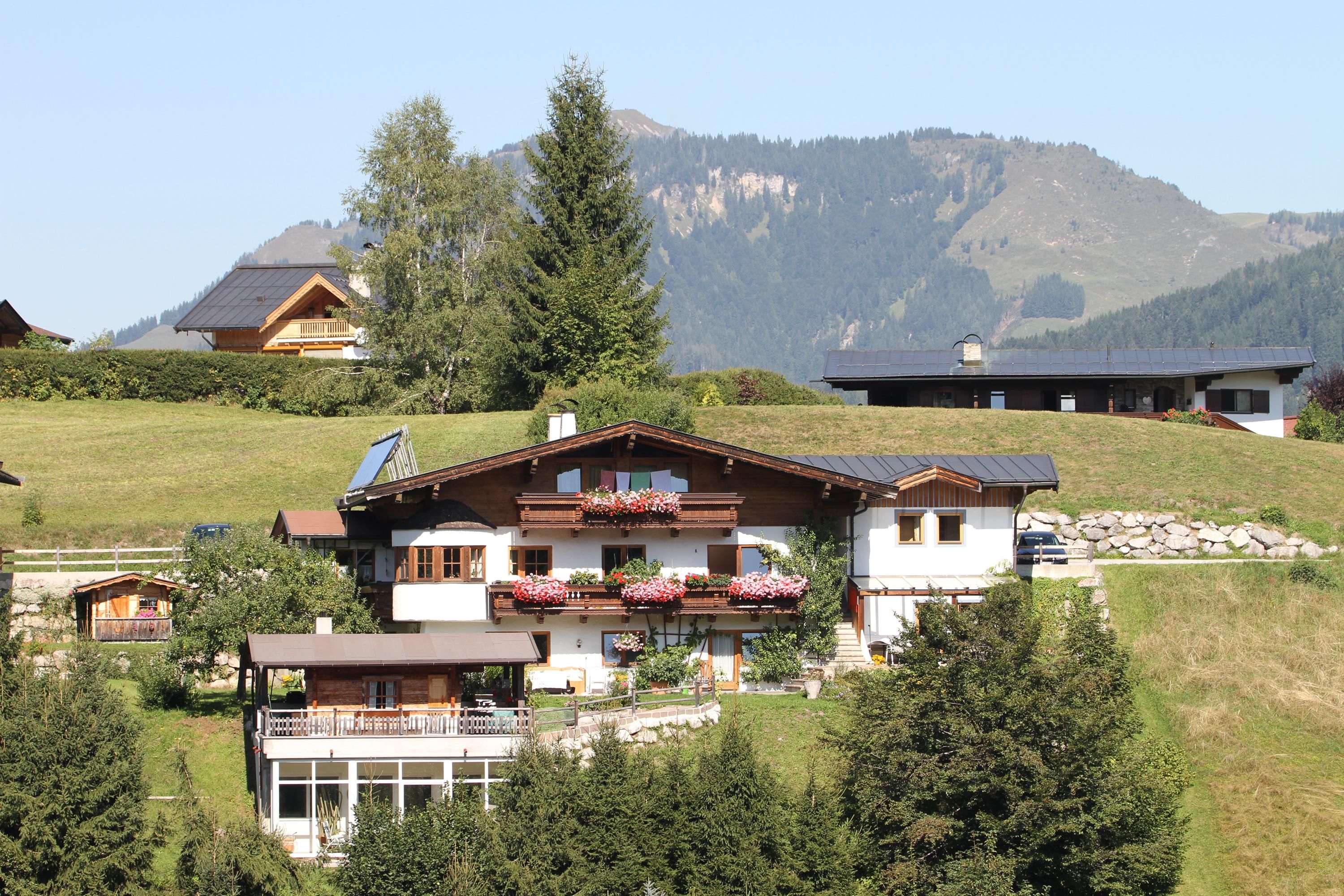 Ein wunderschönes Haus in einer grünen Hügellandschaft. Im Hintergrund sind Berge und ein klarer Himmel zu sehen.