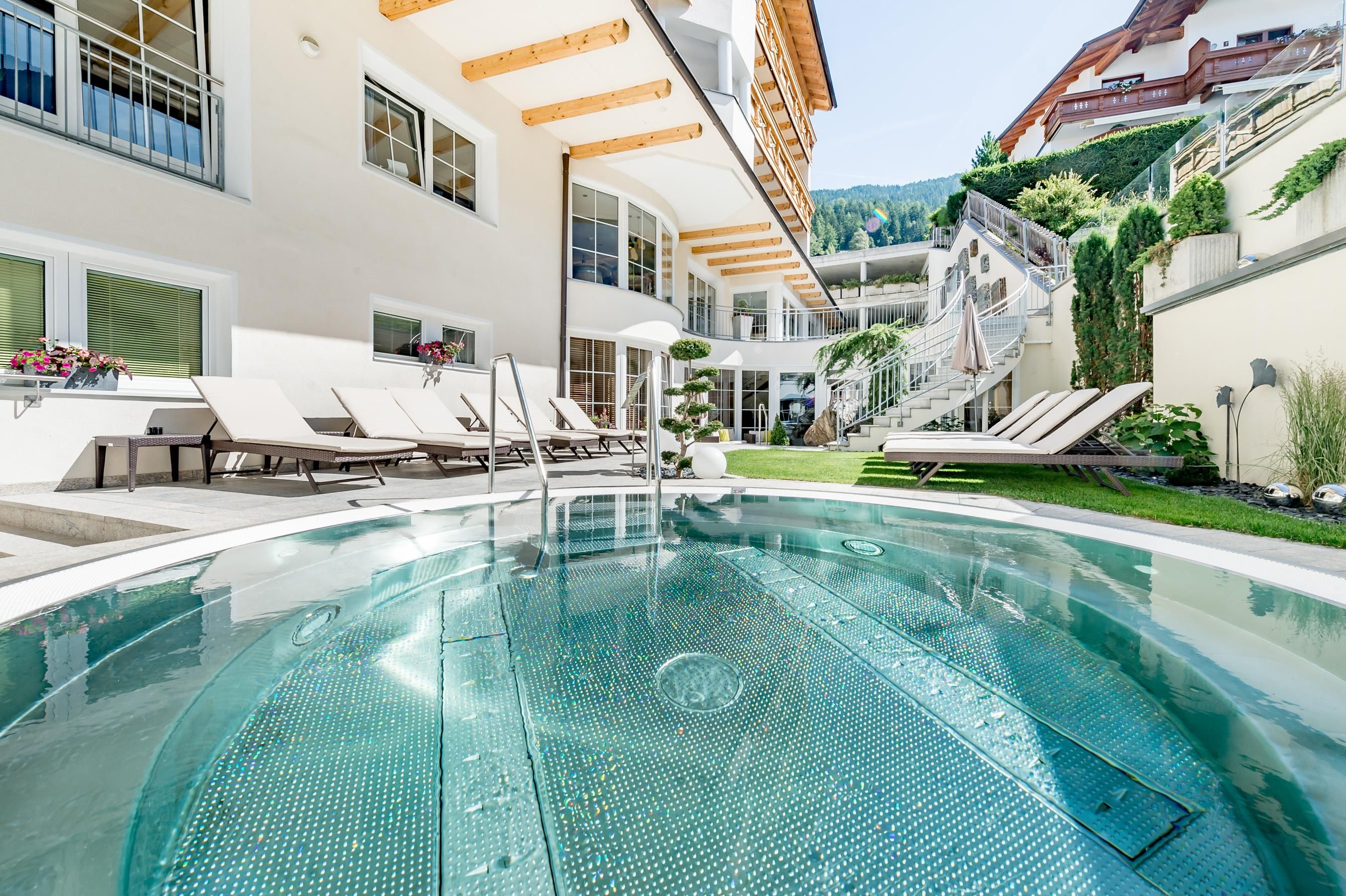 Ein schöner Poolbereich mit modernen Liegen und einer grünen Umgebung. Die Architektur ist hell und einladend, ideal zum Entspannen.