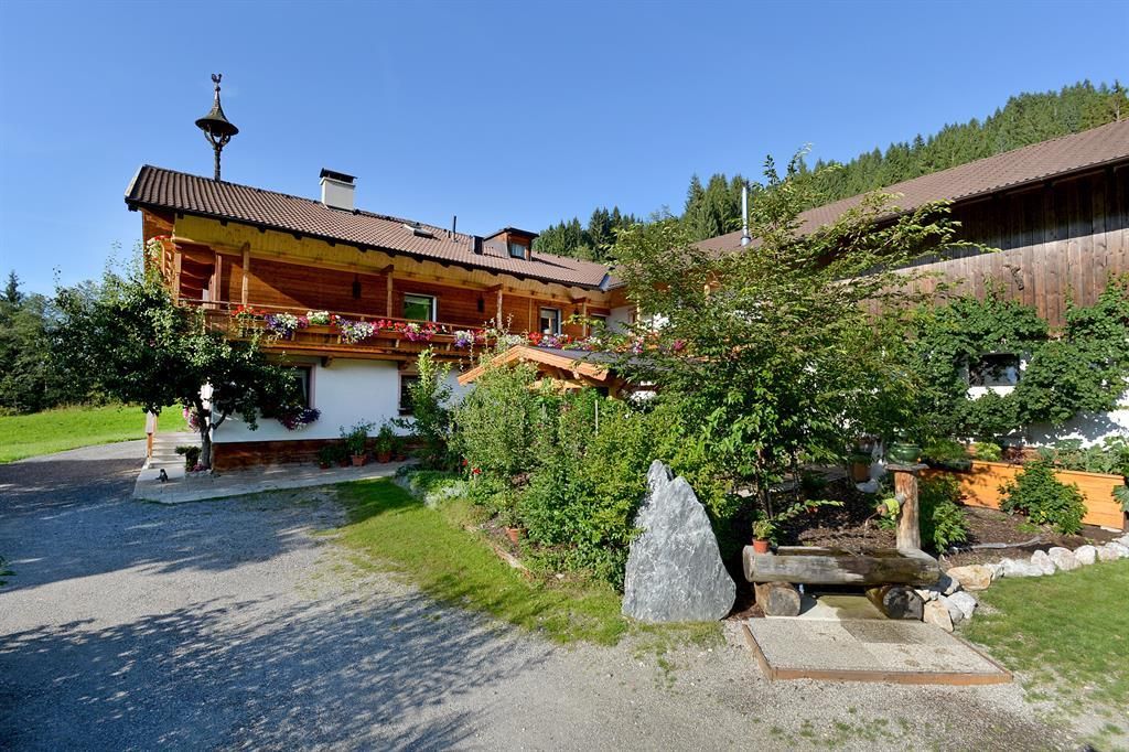 Ein traditionelles Chalet umgeben von grüner Landschaft und Bäumen. Der Garten hat schöne Pflanzen und einen kleinen Brunnen.