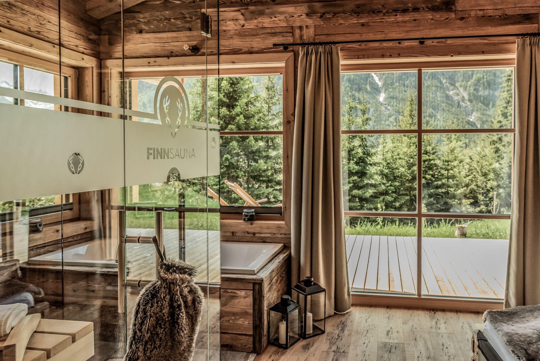 Ein modernes Badezimmer aus Holz mit großen Fenstern und Blick auf die Natur. Die Glaswand zur Sauna und die stilvolle Einrichtung schaffen eine entspannende Atmosphäre.