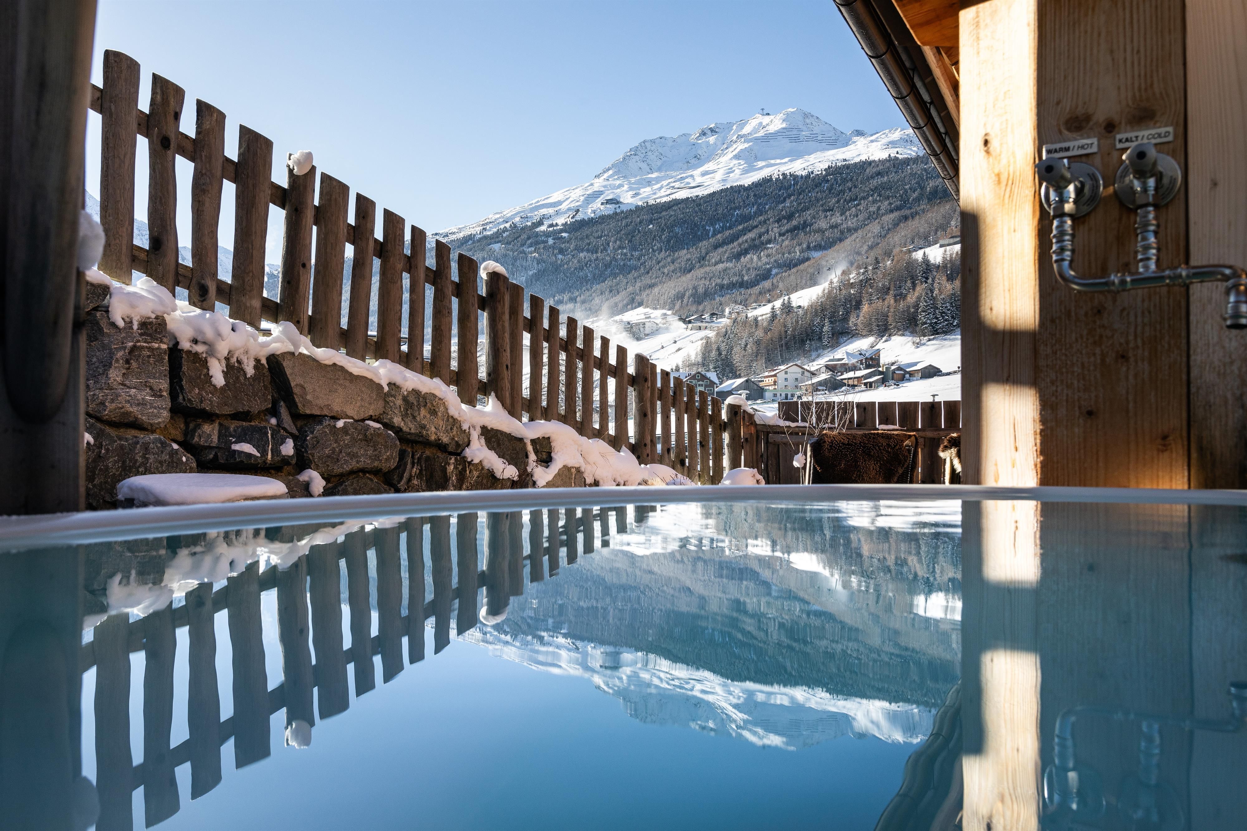 Ein entspannender Außenwhirlpool mit Blick auf schneebedeckte Berge. Die klare Wasseroberfläche spiegelt die schöne Landschaft wider.