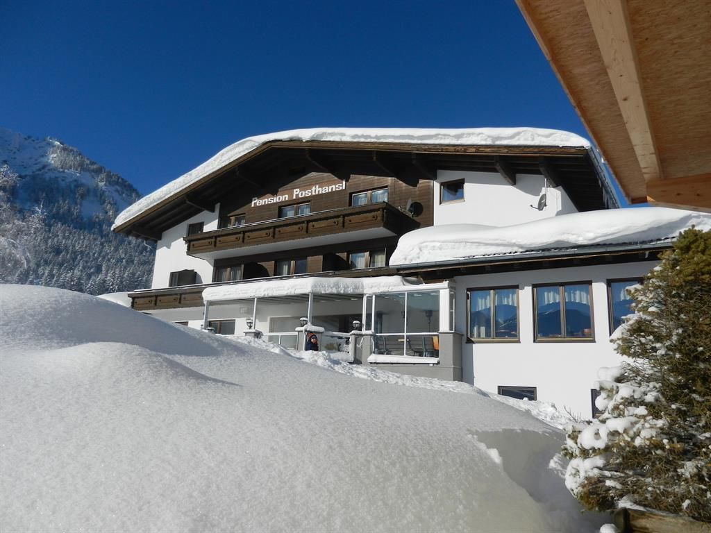 Ein malerisches Gästehaus im Schnee mit einem klaren blauen Himmel. Die Umgebung ist von schneebedeckten Bergen umgeben.