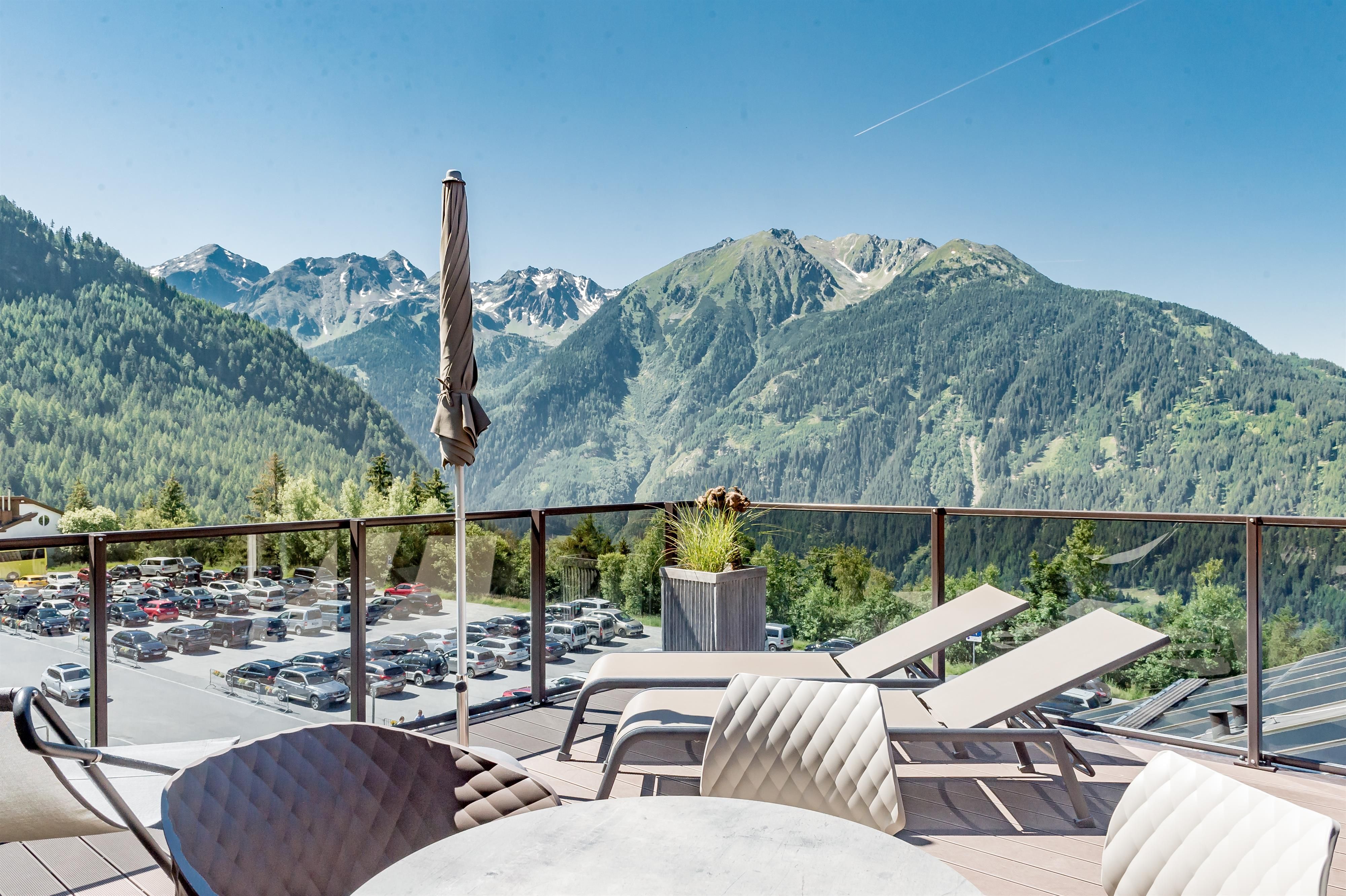 Eine sonnige Terrasse mit Liegen und einem beeindruckenden Blick auf die Berge. Der klare blaue Himmel ergänzt die malerische Landschaft.