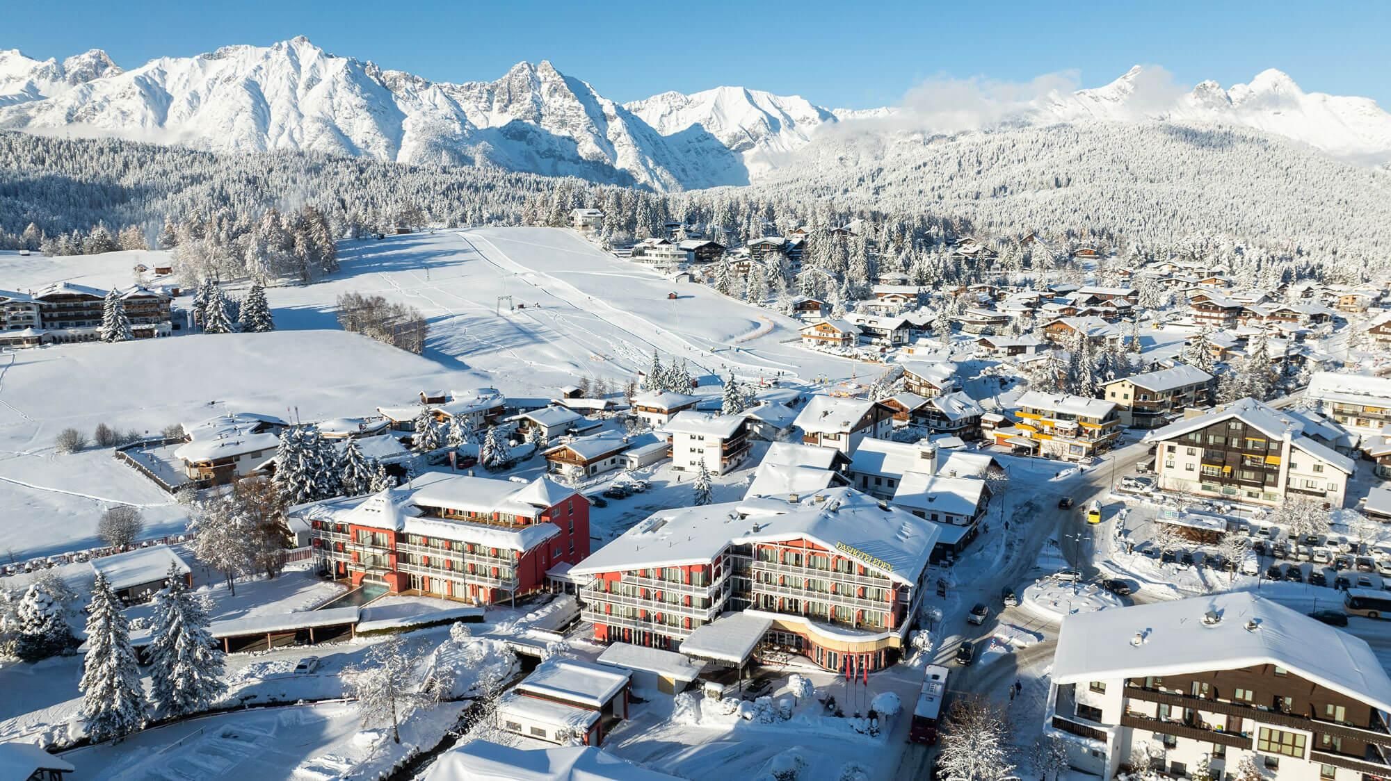 Eine malerische Winterlandschaft mit schneebedeckten Bergen und einem charmanten Dorf. Die Gebäude sind mit Schnee bedeckt und es strahlt eine ruhige, winterliche Atmosphäre aus.