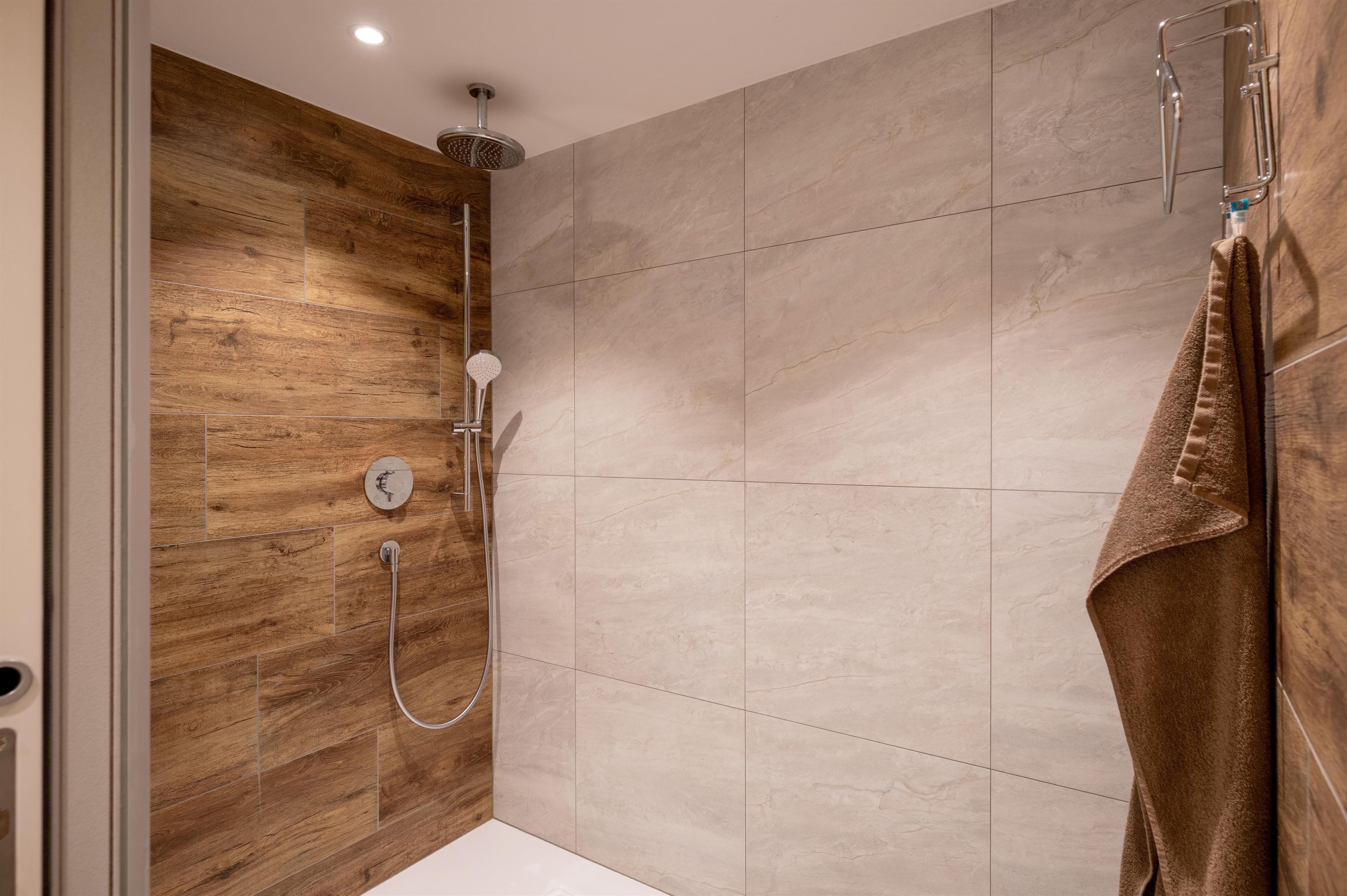 Eine moderne Dusche mit eleganten Fliesen und Holzverkleidung. Handtuch hängt an der Wand neben der Dusche.