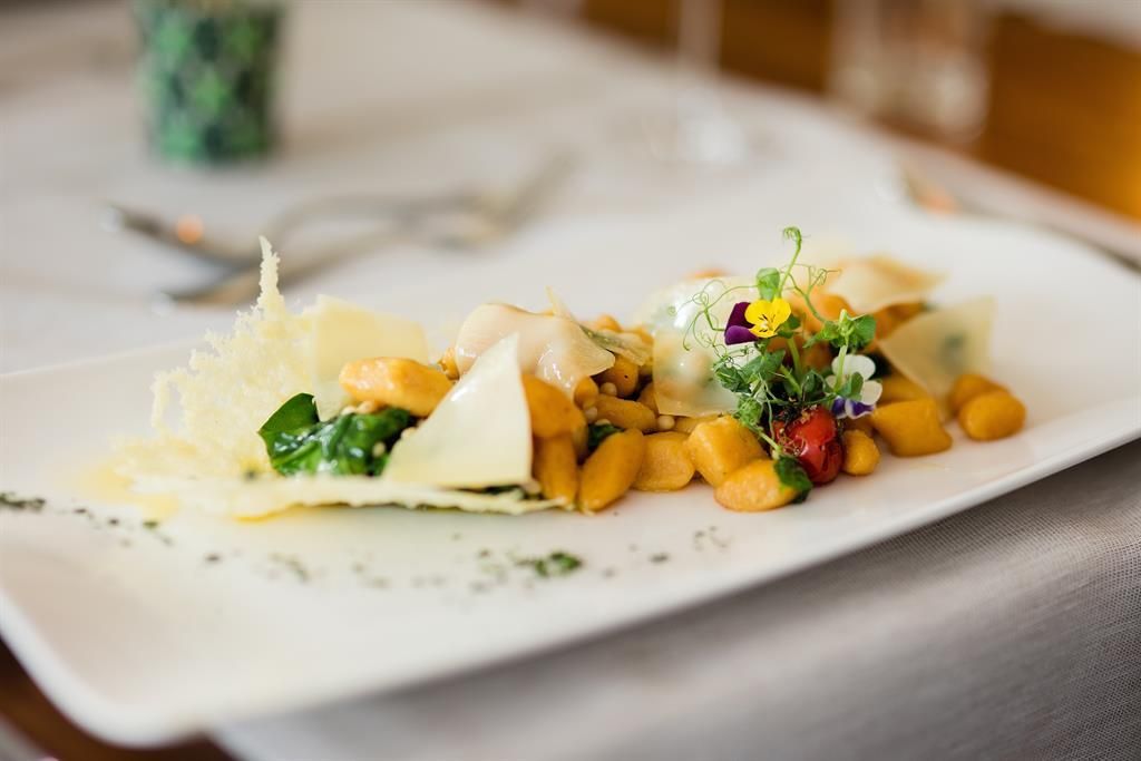 Ein elegantes Gericht mit knusprigem Käse, frischen Kräutern und buntem Gemüse. Die Gnocchi sind sorgfältig angerichtet und wirken sehr appetitlich.