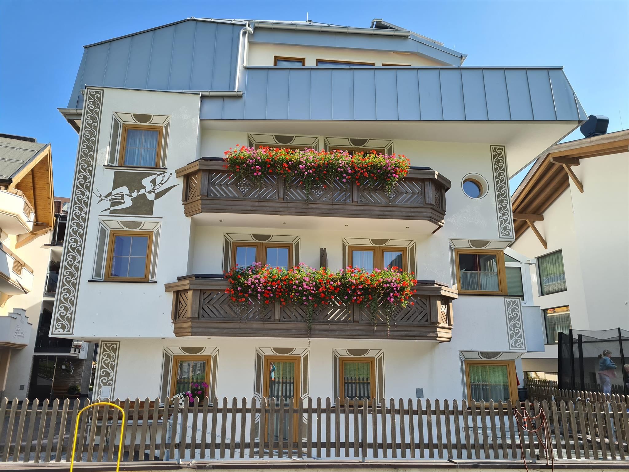 Ein schönes Haus mit Balkonen, die mit bunten Blumen geschmückt sind. Der klare Himmel fügt eine freundliche Atmosphäre hinzu.