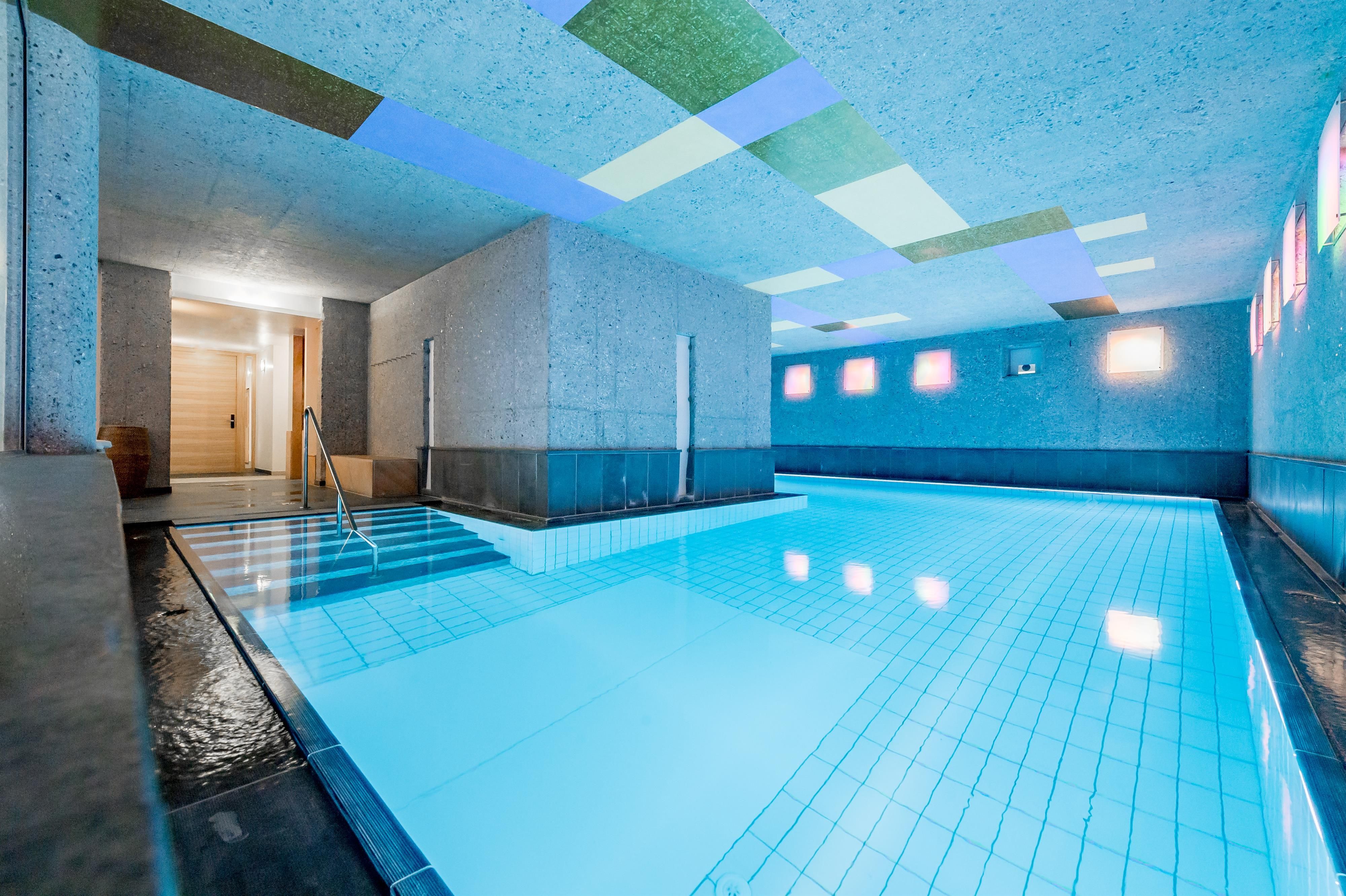 Ein modernes Schwimmbad mit klarem, blauem Wasser und einem eleganten Design. Das Licht fällt durch die bunten Fenster und schafft eine entspannende Atmosphäre.