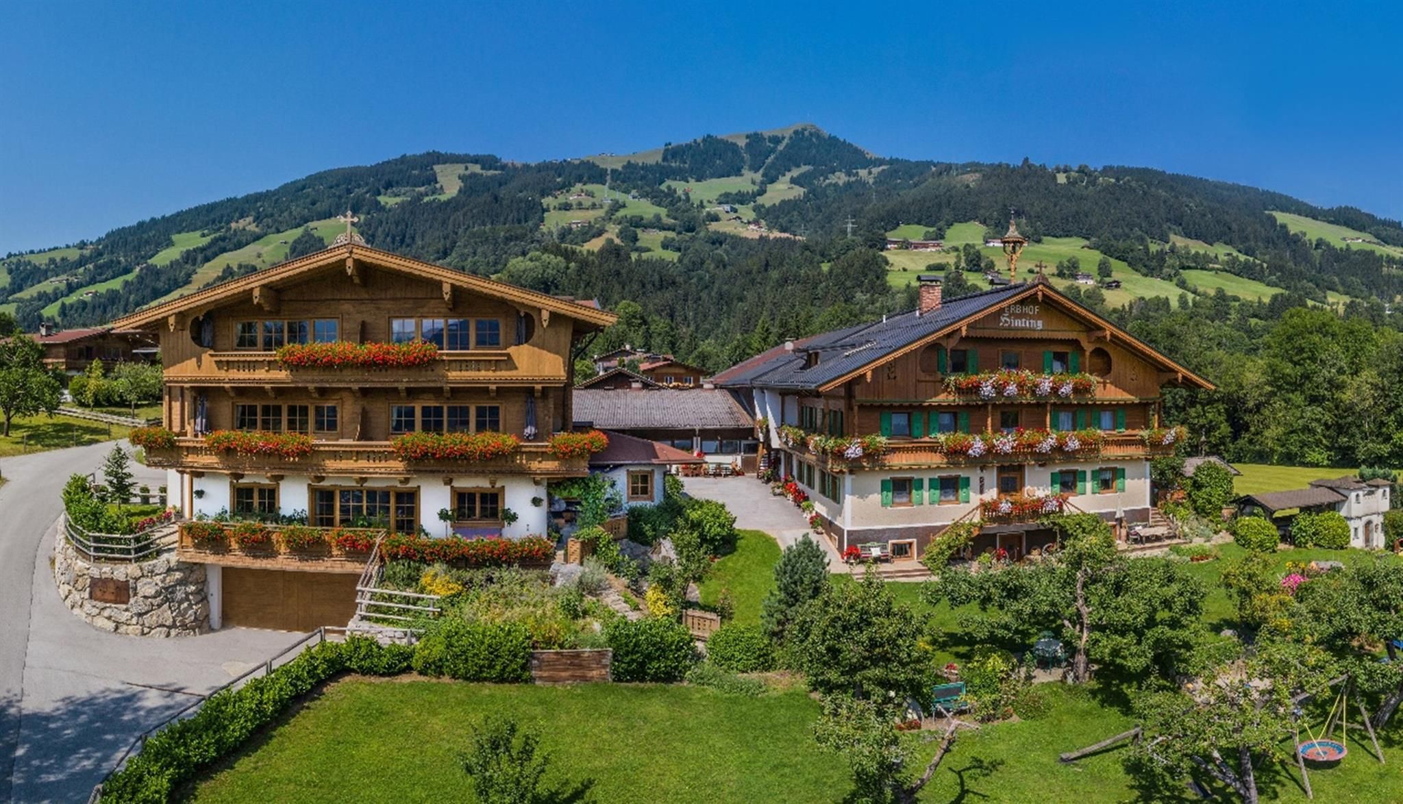 Ein malerisches Alpenhaus mit Holzverkleidung und bunten Balkonen. Im Hintergrund erheben sich grüne Hügel unter einem klaren blauen Himmel.
