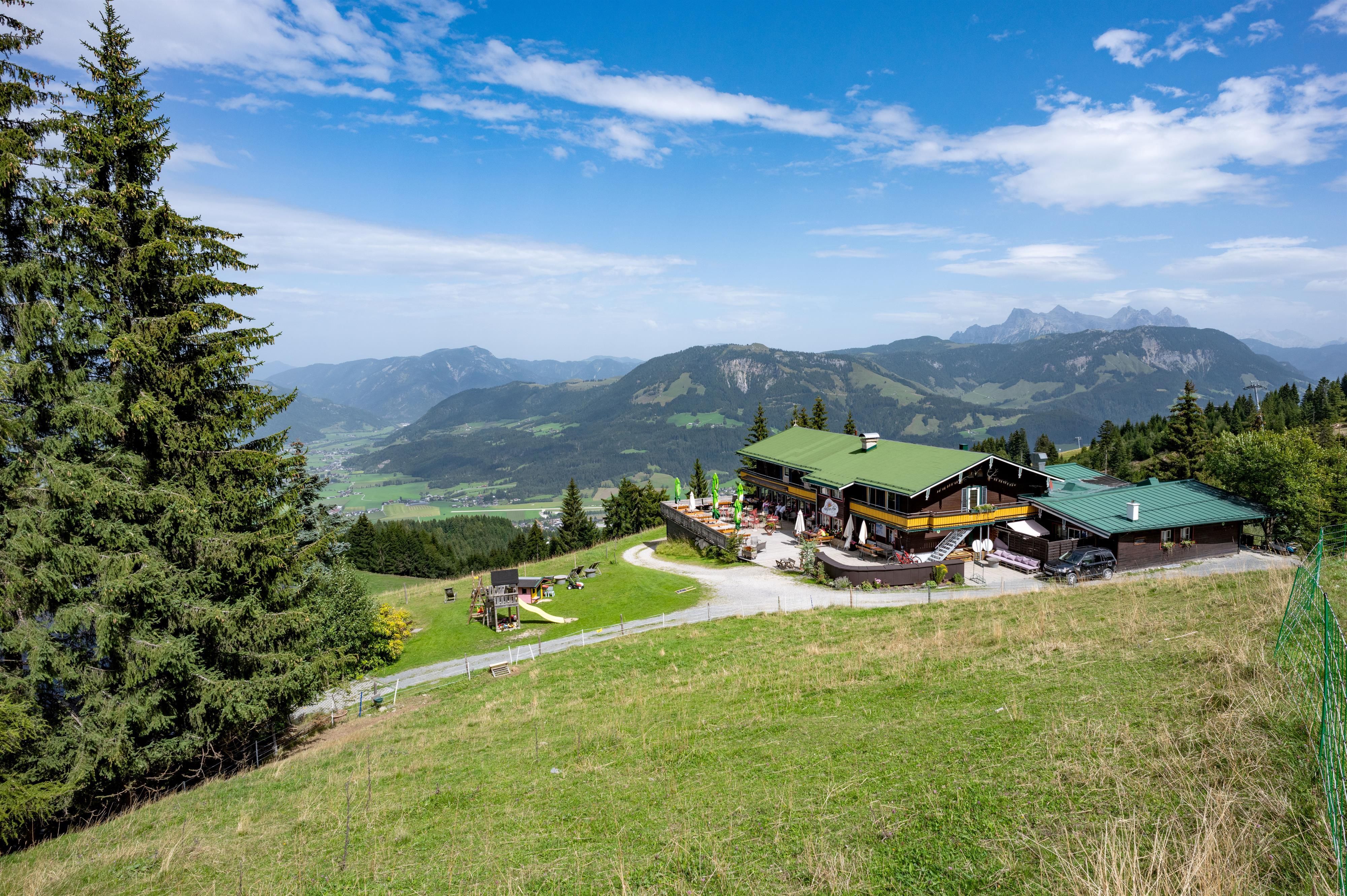 Eine malerische Berglandschaft mit einem gemütlichen Restaurant im Vordergrund. Im Hintergrund sind grüne Hügel und eine klare blaue Sky zu sehen.