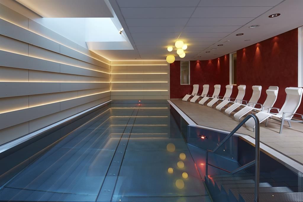Ein eleganter Wellnessbereich mit einem klaren Schwimmbecken und modernen Liegen. Sanftes Licht schafft eine entspannende Atmosphäre.