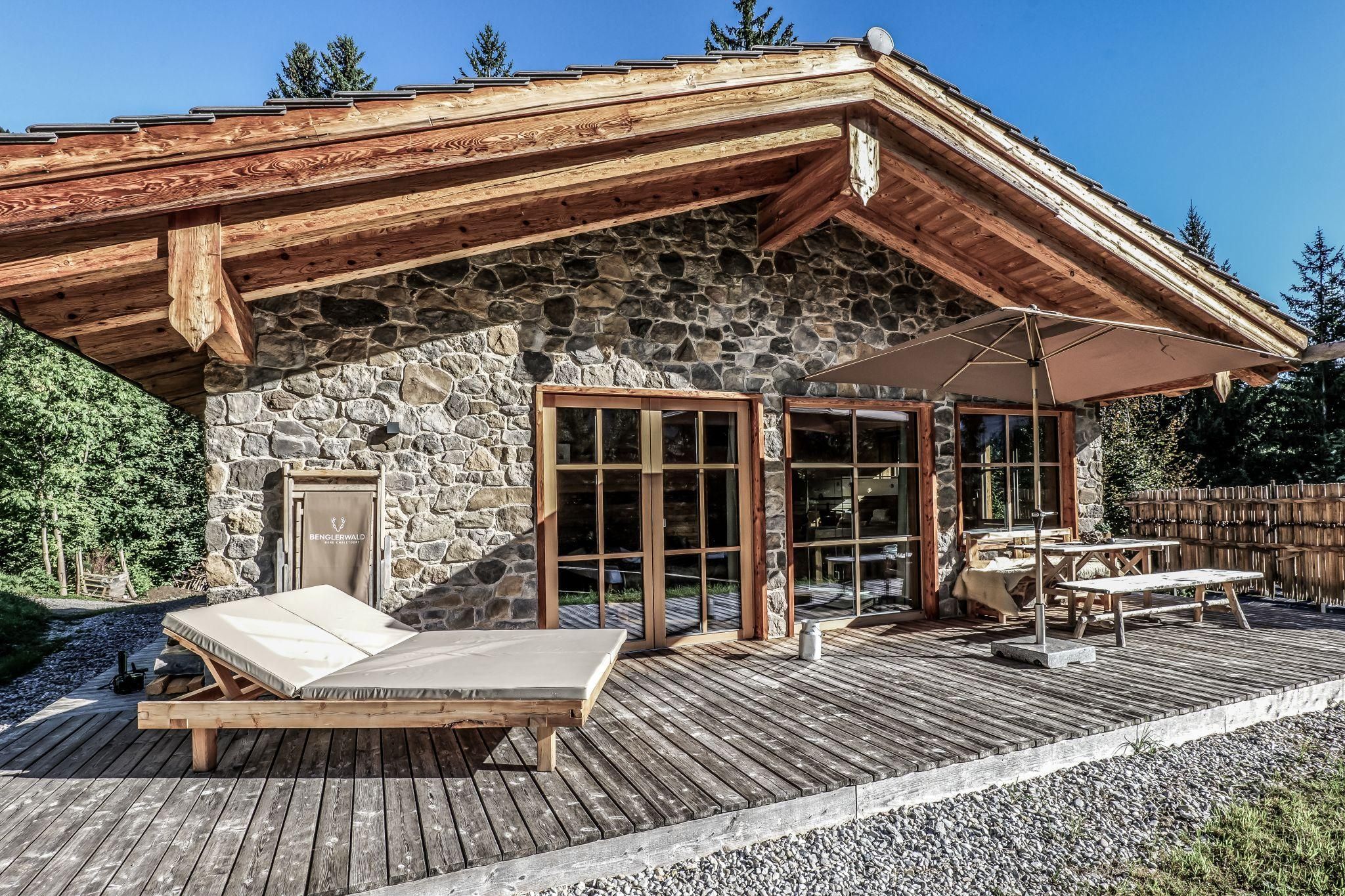 Ein gemütliches Stein Chalet umgeben von Natur. Die Terrasse ist mit Liegen und einem Tisch ausgestattet.