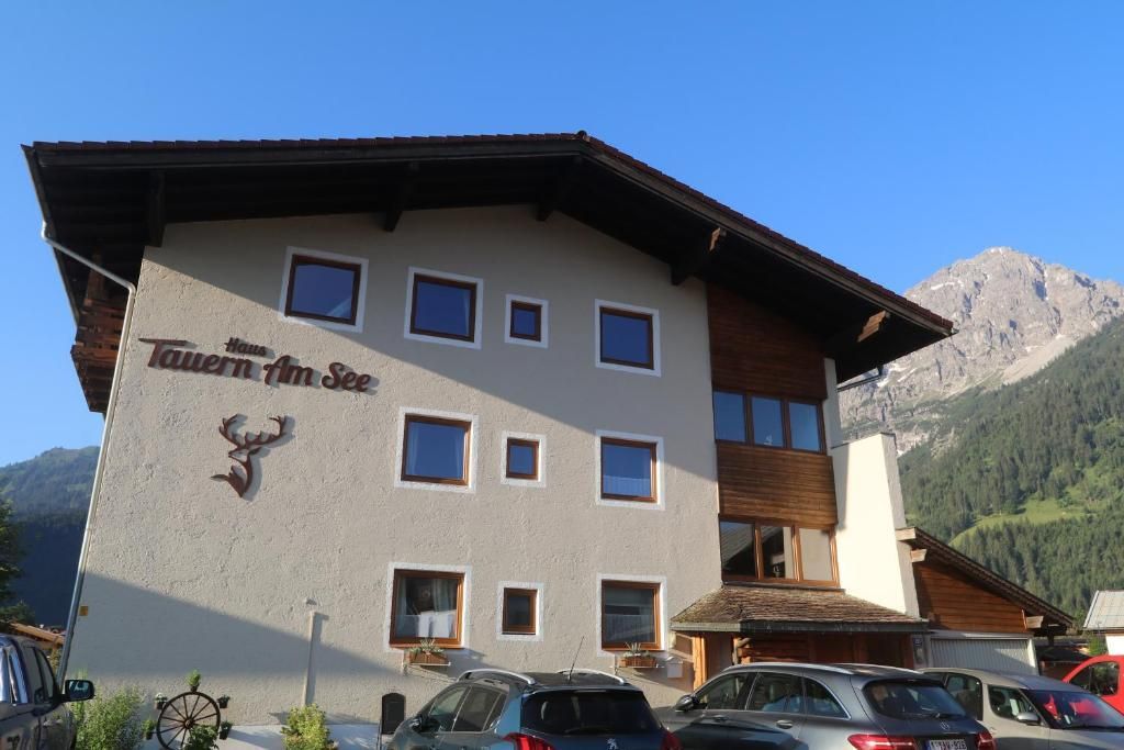 Ein gemütliches Gasthaus namens "Tavern am See" mit modernen Fenstern und einem schönen Bergblick. Parkplätze sind vor dem Gebäude vorhanden.
