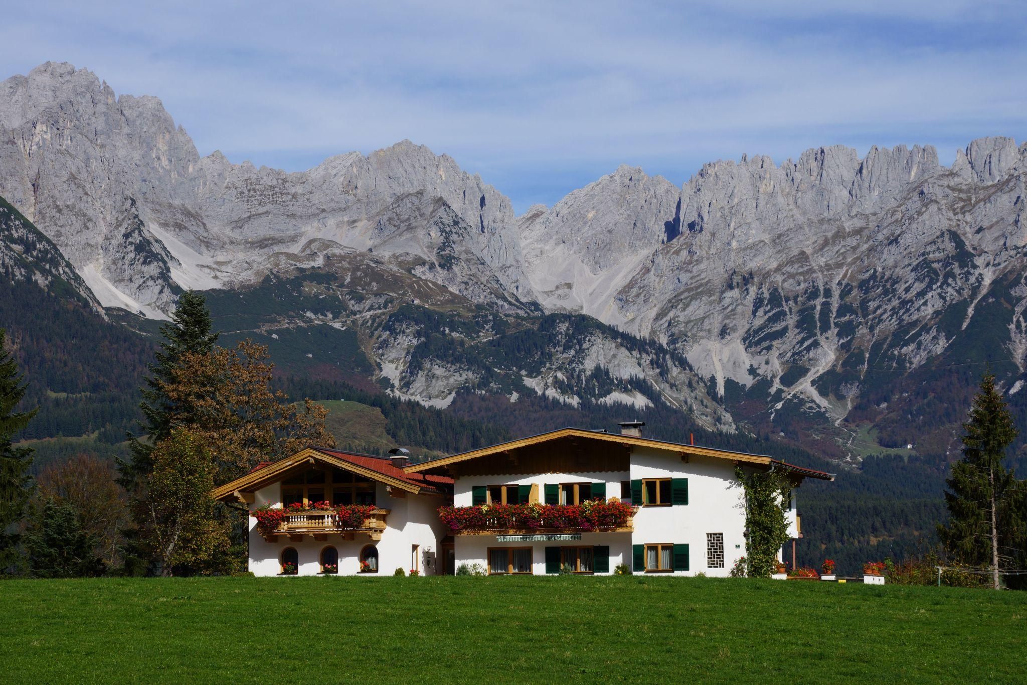 Ein schönes Haus in den Alpen, umgeben von grünen Wiesen und beeindruckenden Bergen. Der Himmel ist klar und die Natur strahlt Ruhe aus.