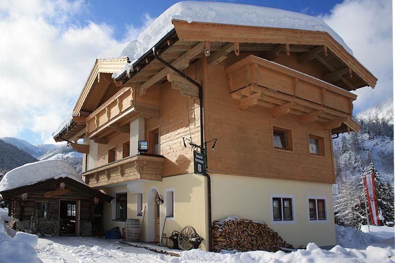 Ein charmantes Holzhaus im Schnee mit einem traditionellen, alpinen Stil. Im Hintergrund sind Berge und ein blauer Himmel zu sehen.